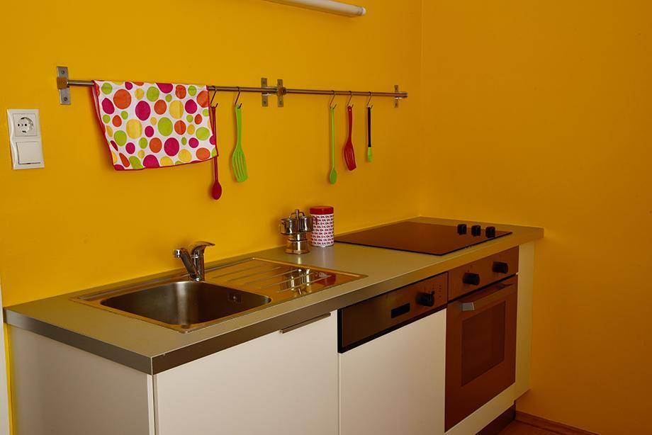 Kompakte Küchenzeile mit gelben Wänden, Spüle, Kochfeld und Backofen, ideal für kleine Wohnungen.