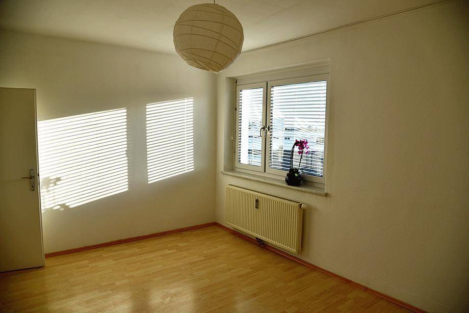Heller Raum mit Parkettboden, Fenster mit Jalousien und Deckenleuchte.