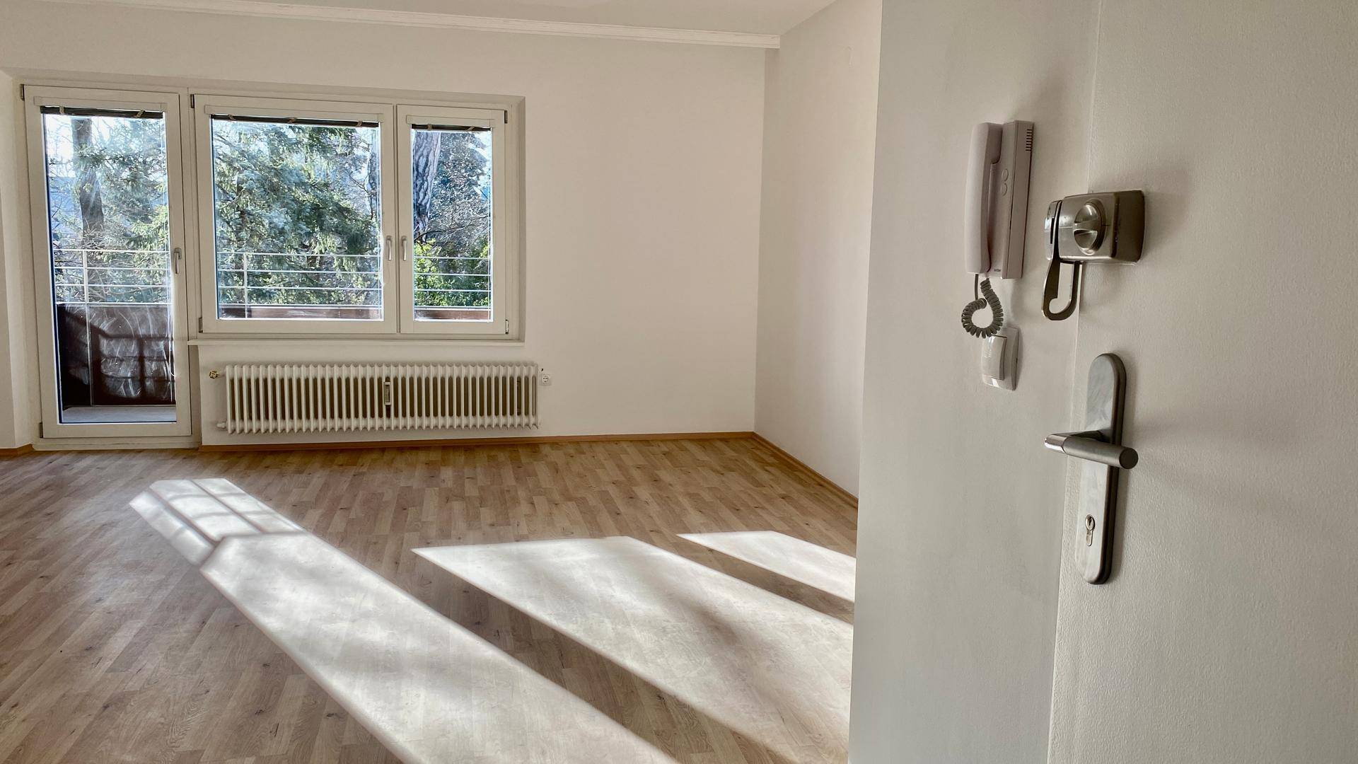 Helles Wohnzimmer mit Parkettboden und Zugang zum Balkon, durchflutet von Sonnenlicht.