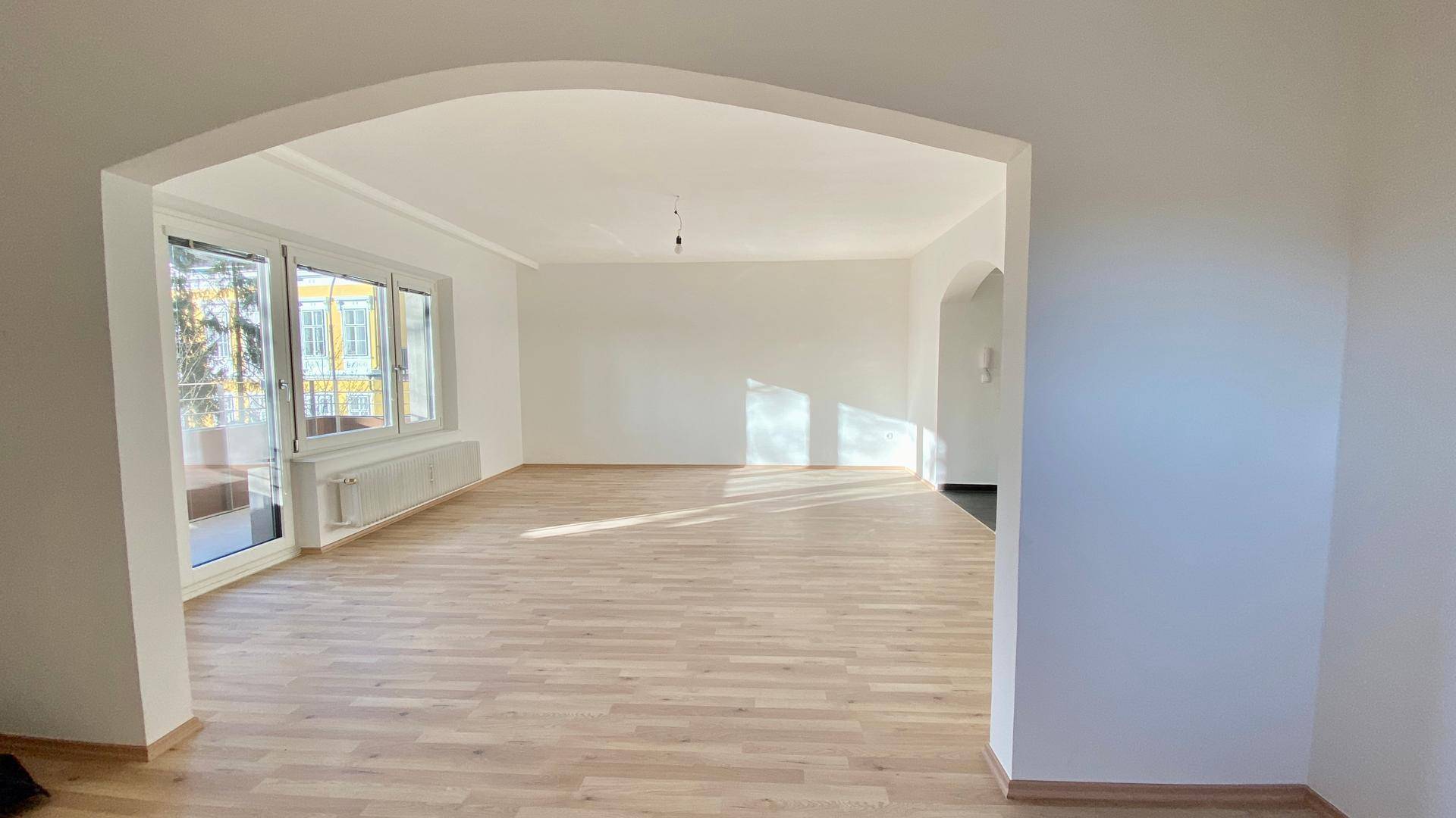 Lichtdurchflutetes Wohnzimmer mit Parkettboden und großem Fenster mit Balkonzugang.