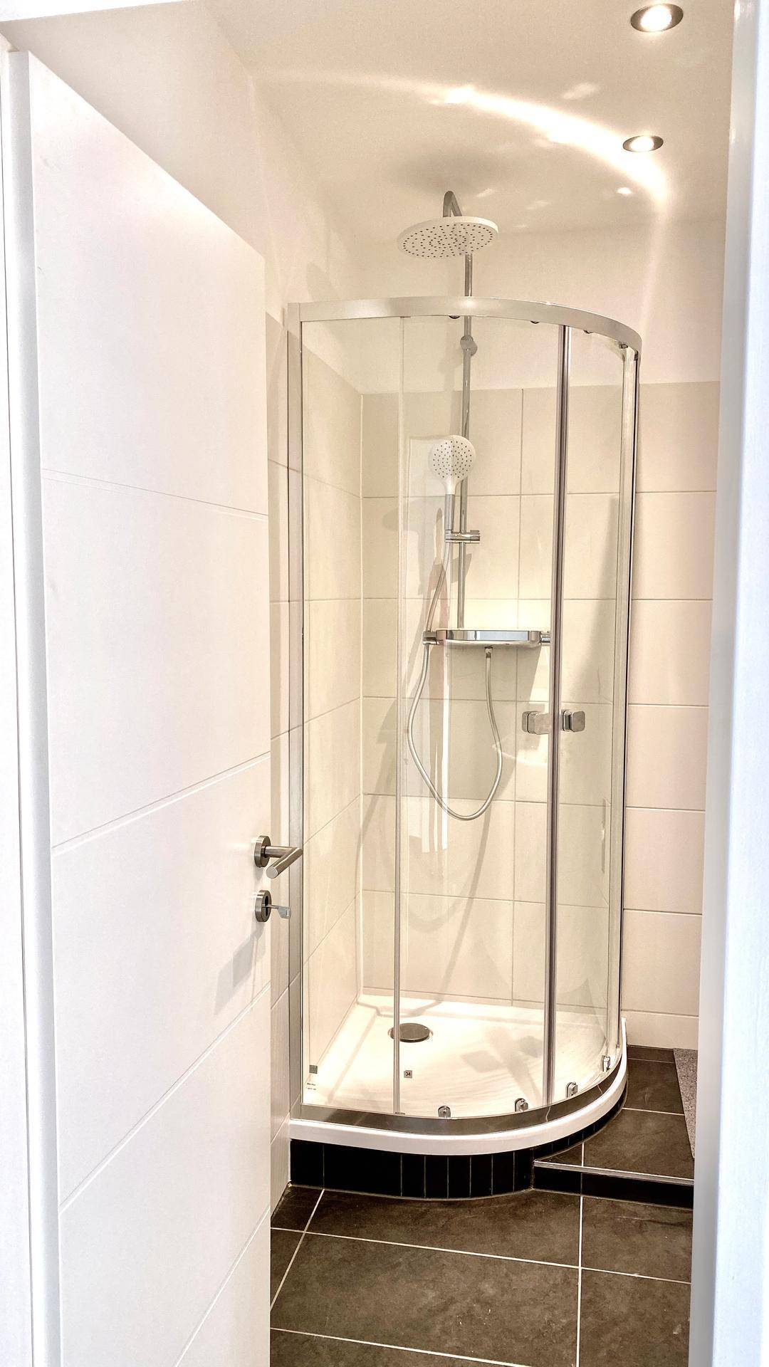 Moderne Duschkabine mit Glaswänden und Regenduschkopf in einem hellen Badezimmer.