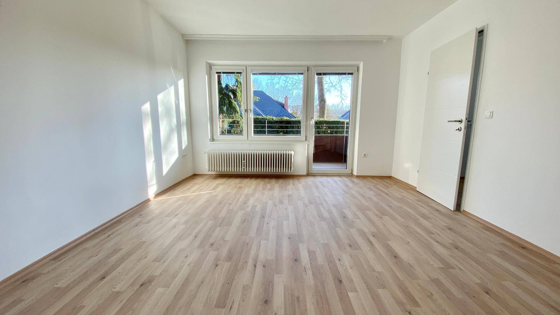 Helles Schlafzimmer mit Parkettboden und Balkonzugang, durchflutet von Sonnenlicht.