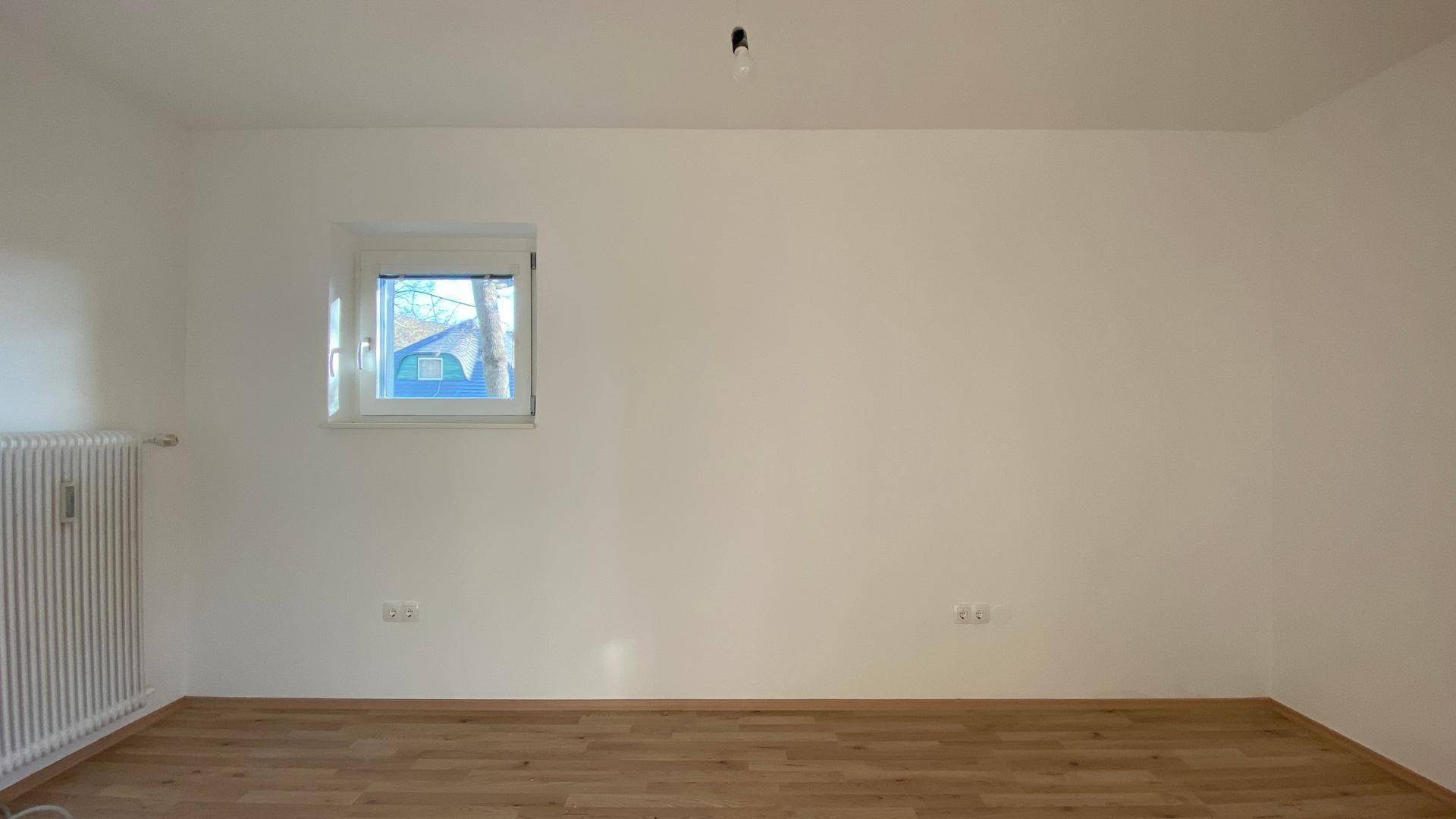 Wand im Wohnzimmer mit einem Fenster und Heizkörper, bietet Blick ins Grüne.