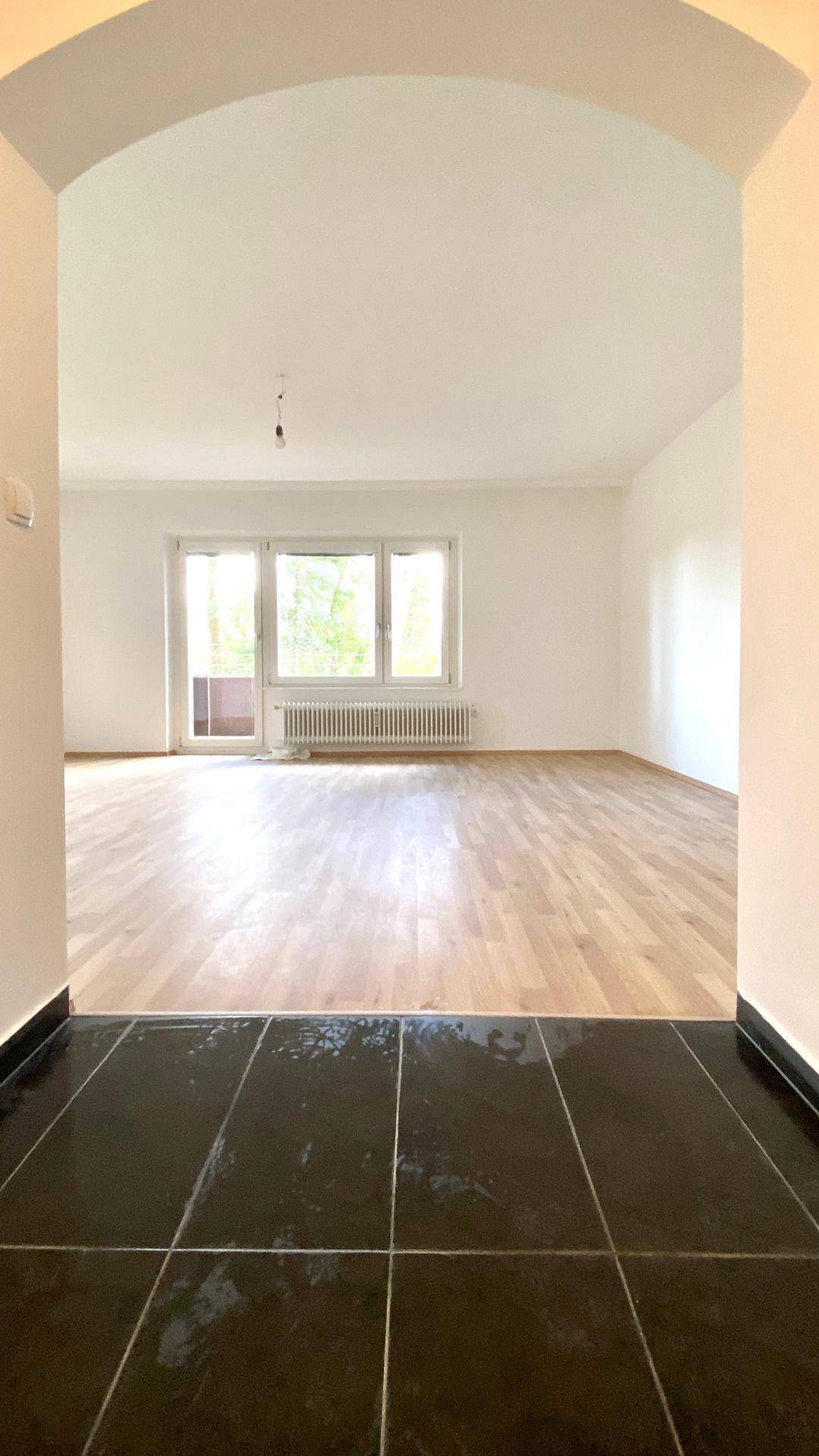 Heller Eingangsbereich mit dunklen Fliesen, der in ein geräumiges Wohnzimmer mit Parkettboden übergeht.