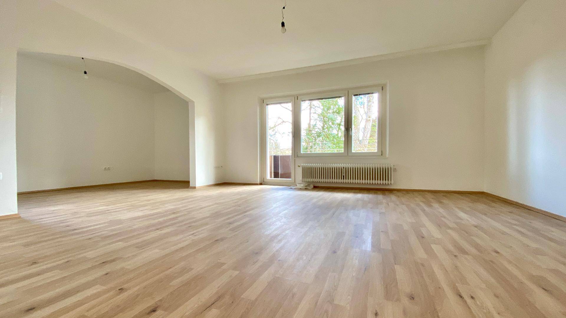 Großzügiges Wohnzimmer mit hellem Parkettboden und direktem Zugang zum Balkon.
