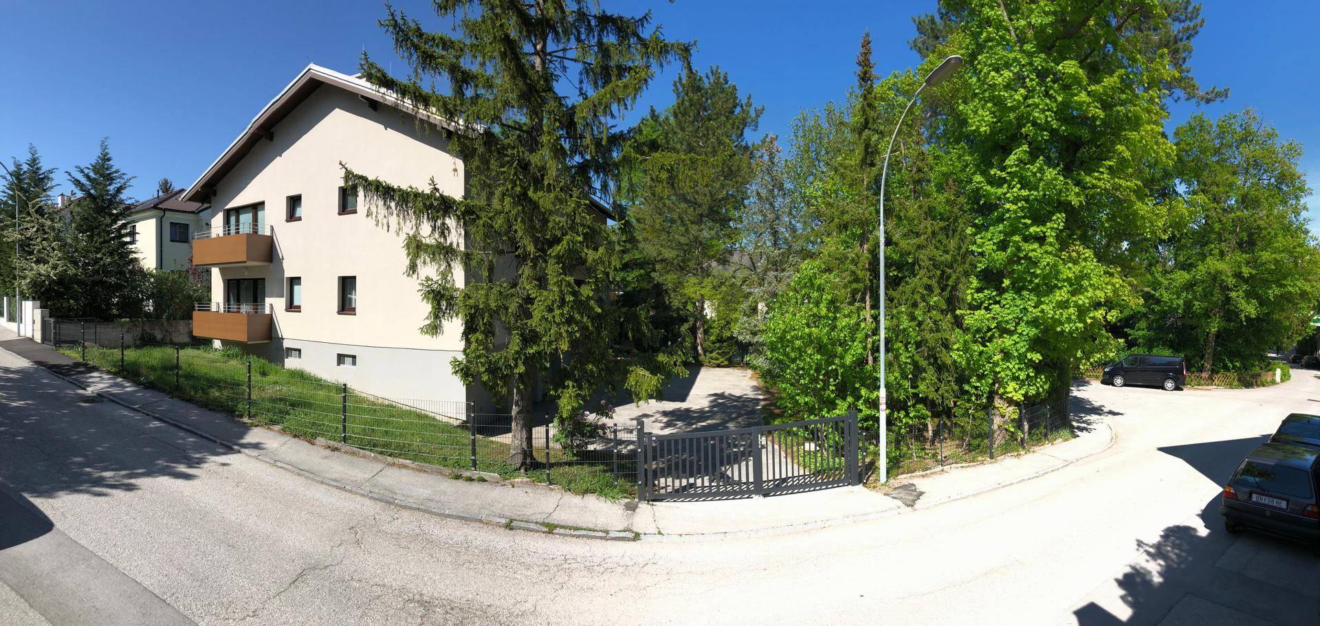 Weitwinkelansicht des Gebäudes und der ruhigen Wohnstraße mit viel Grün und Bäumen.