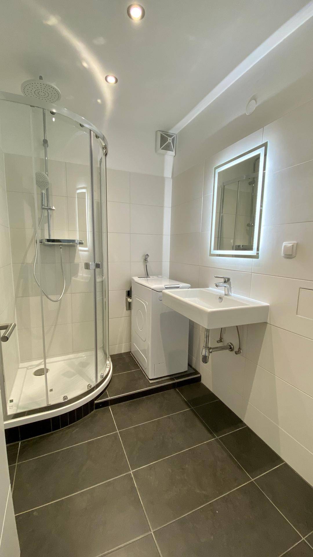 Modernes Badezimmer mit Duschkabine, Waschbecken und Platz für eine Waschmaschine.