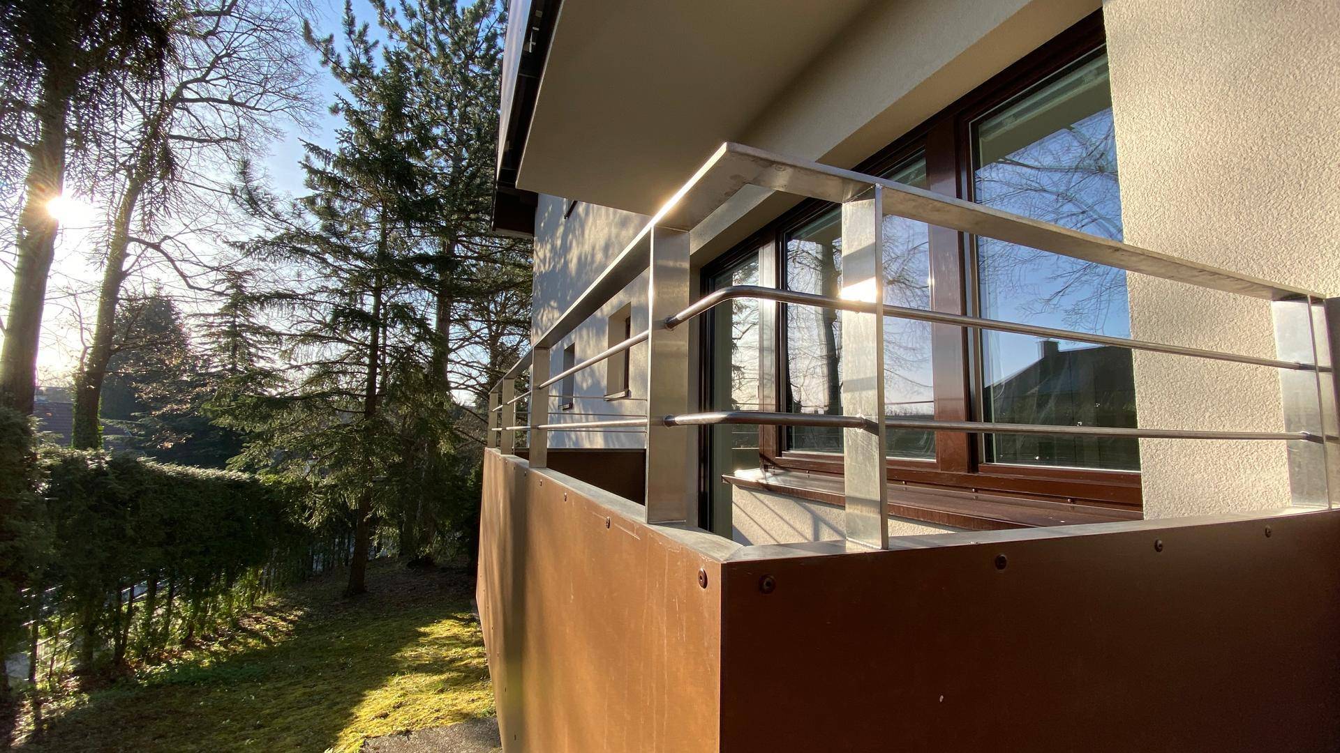 Detailansicht des Balkons mit modernem Metallgeländer und Sonnenlicht durch die Bäume.