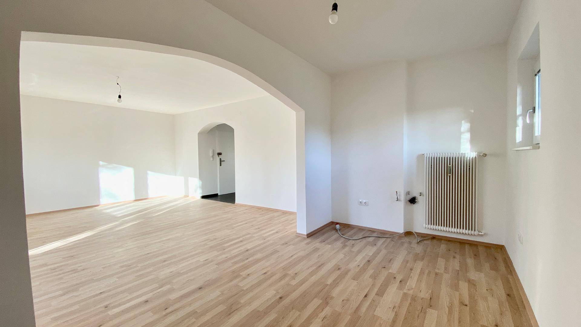 Geräumiger Wohnbereich mit Parkettboden, der durch einen Bogen zum Eingangsbereich führt.
