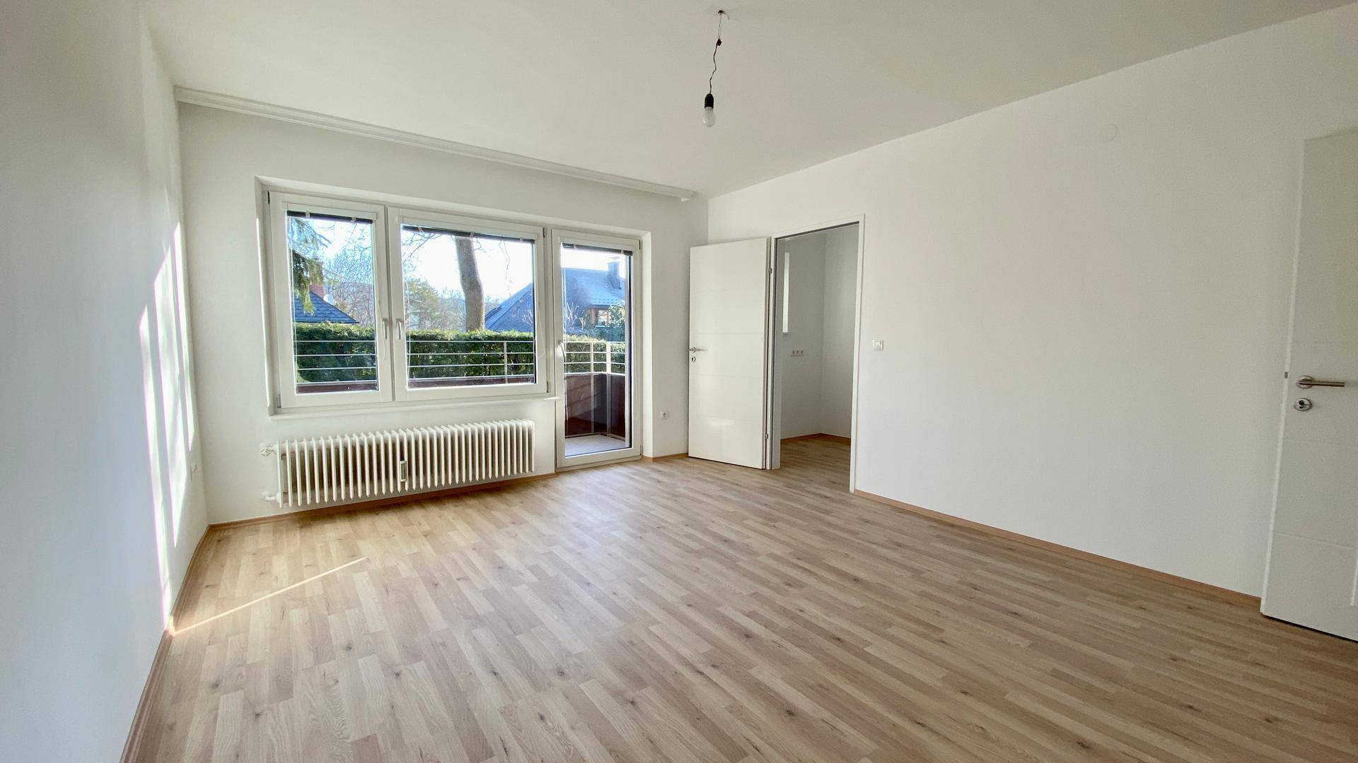 Geräumiges Schlafzimmer mit Parkettboden und großem Fenster mit Zugang zum Balkon.