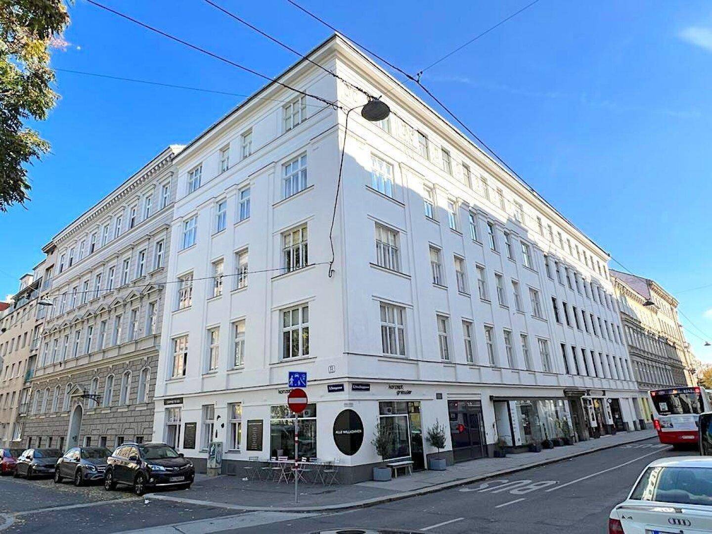 Modernes Eckgebäude mit weißer Fassade und großen Fenstern in einer städtischen Umgebung.