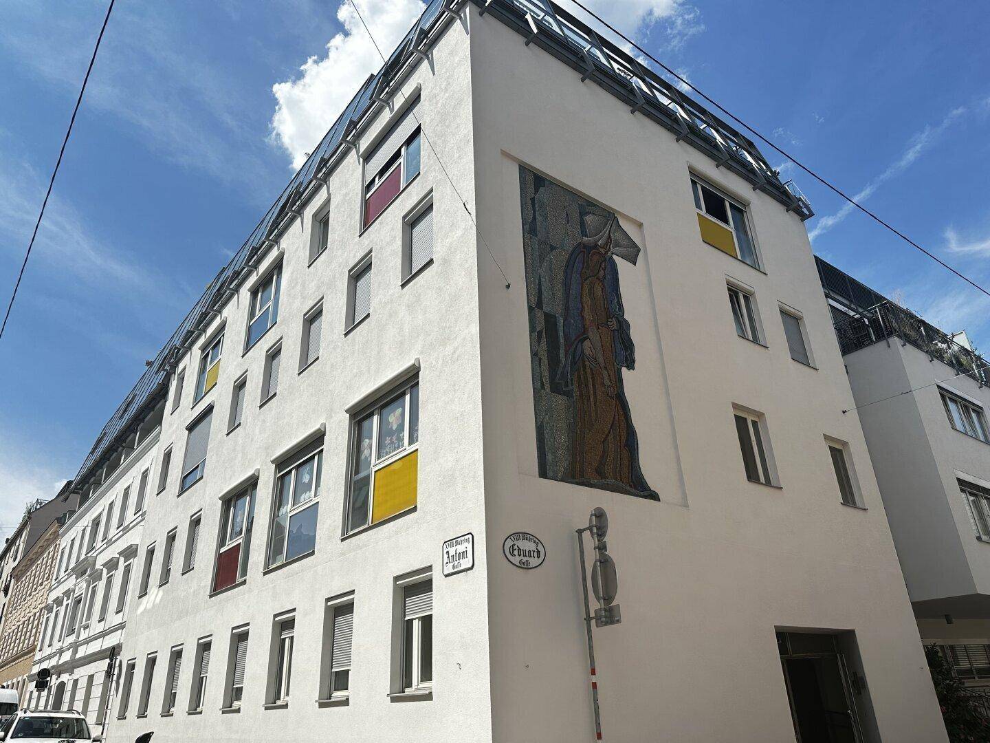 Modernes Mehrfamilienhaus mit weißer Fassade, farbigen Fensterrahmen und einem großen Wandgemälde.