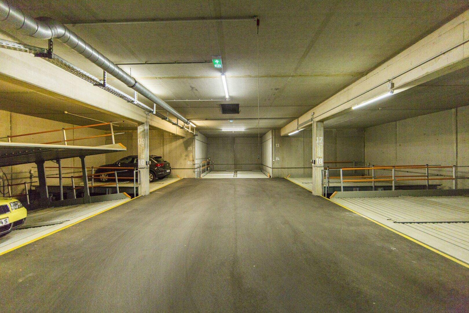 Geräumige Tiefgarage mit mehreren mechanischen Parksystemen und sichtbaren Versorgungsleitungen.