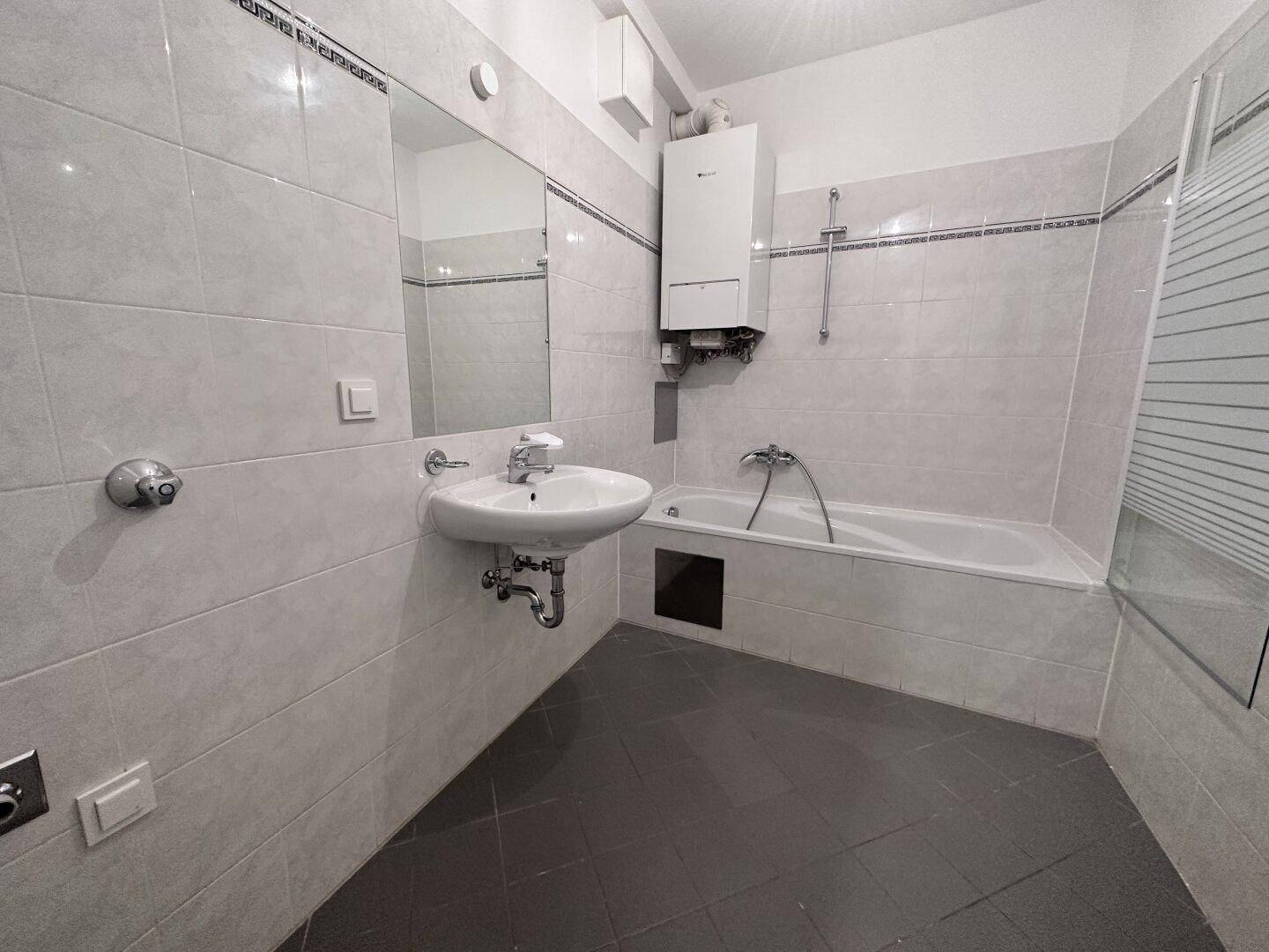 Badezimmer mit Badewanne, Waschbecken und hellen Fliesen an den Wänden.