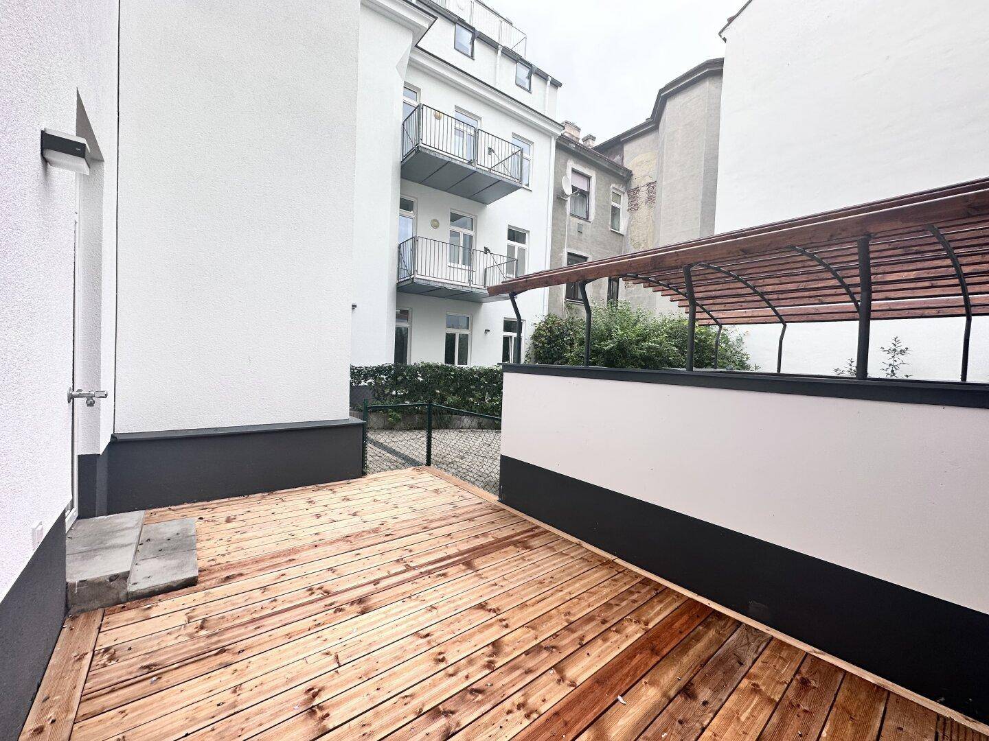 Holzterrasse mit Überdachung und Blick auf den Innenhof des Gebäudes.