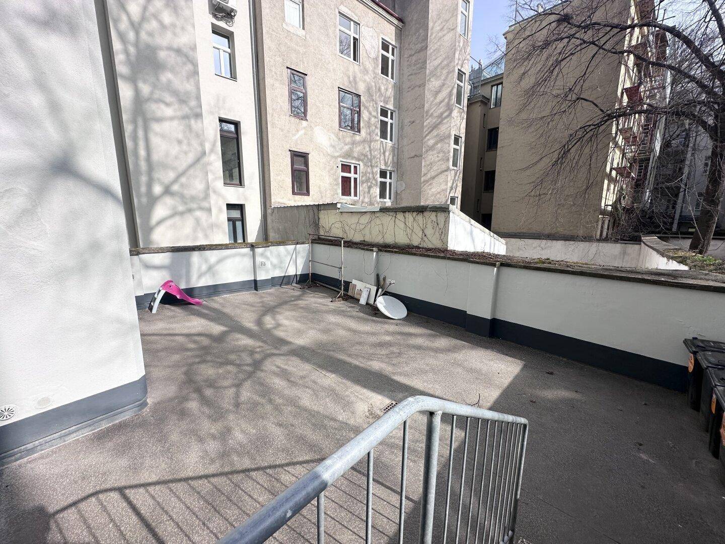Unmöblierte Außenterrasse mit Blick auf umliegende Gebäude.