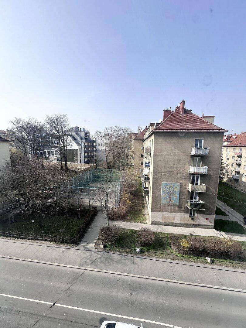 Blick aus dem Fenster auf eine städtische Straße, Gebäude und einen Sportplatz.