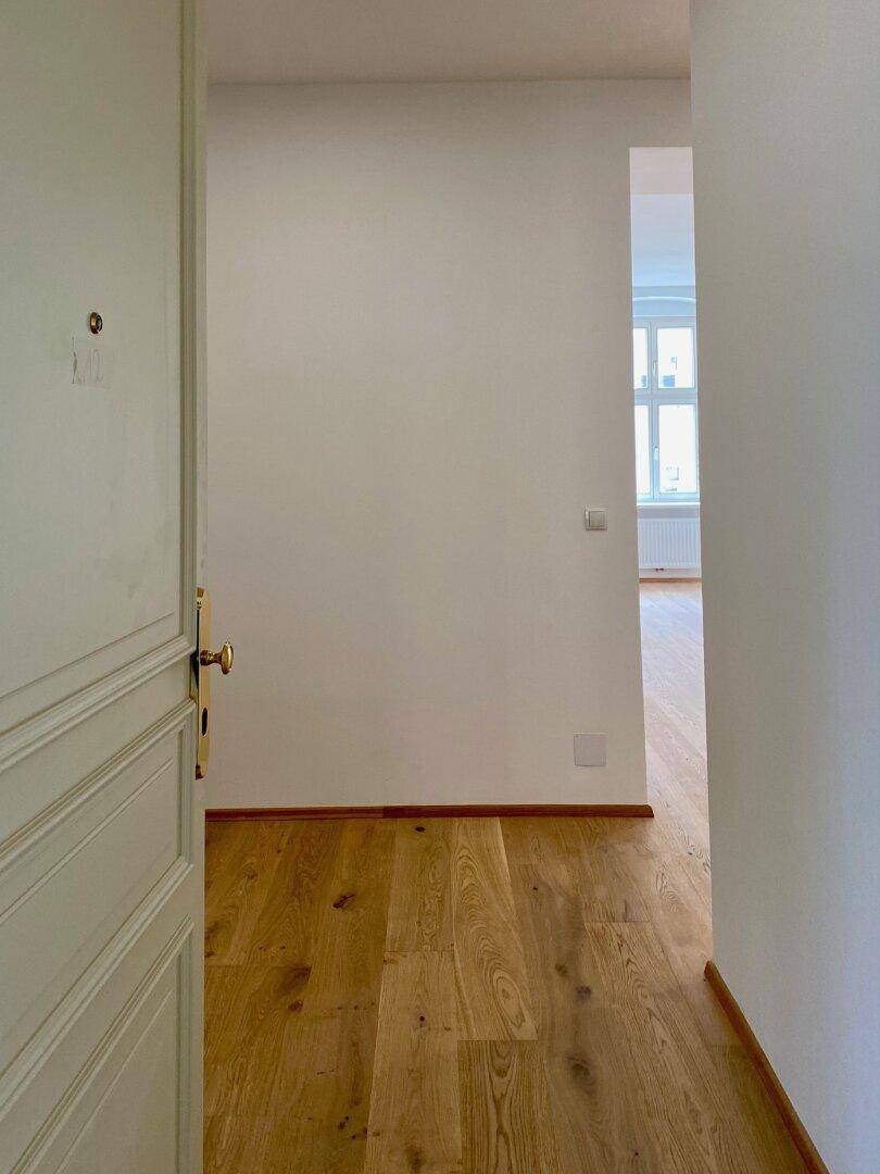 Heller Flur mit Holzboden und einer geöffneten Eingangstür, die in die Wohnung führt.