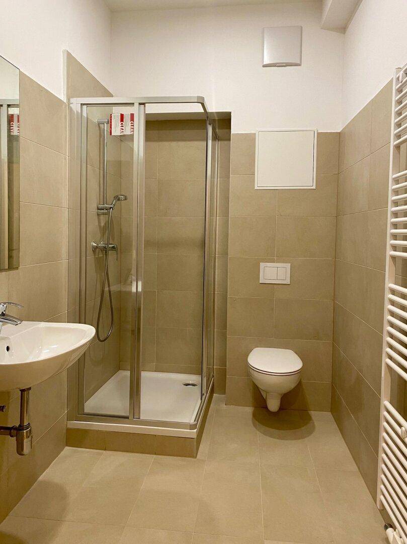 Modernes Badezimmer mit Dusche, WC, Waschbecken und beheiztem Handtuchhalter in beigen Fliesen.