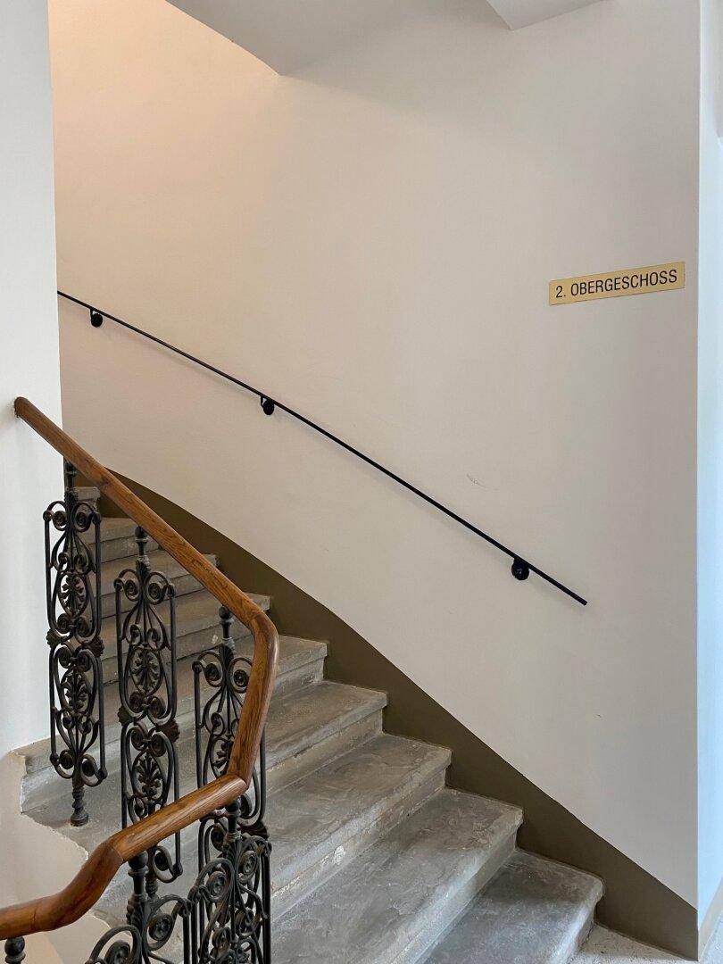 Historisches Treppenhaus mit Steinstufen, schmiedeeisernem Geländer und Holzhandlauf im Altbau.