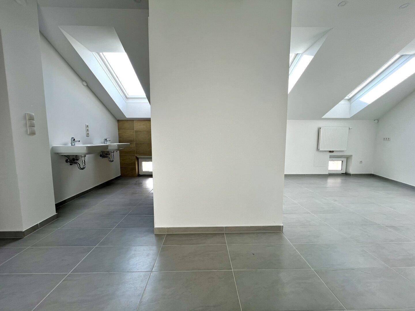 Geräumiges Badezimmer mit zwei Waschbecken und Dachfenstern, in neutralen Farben.