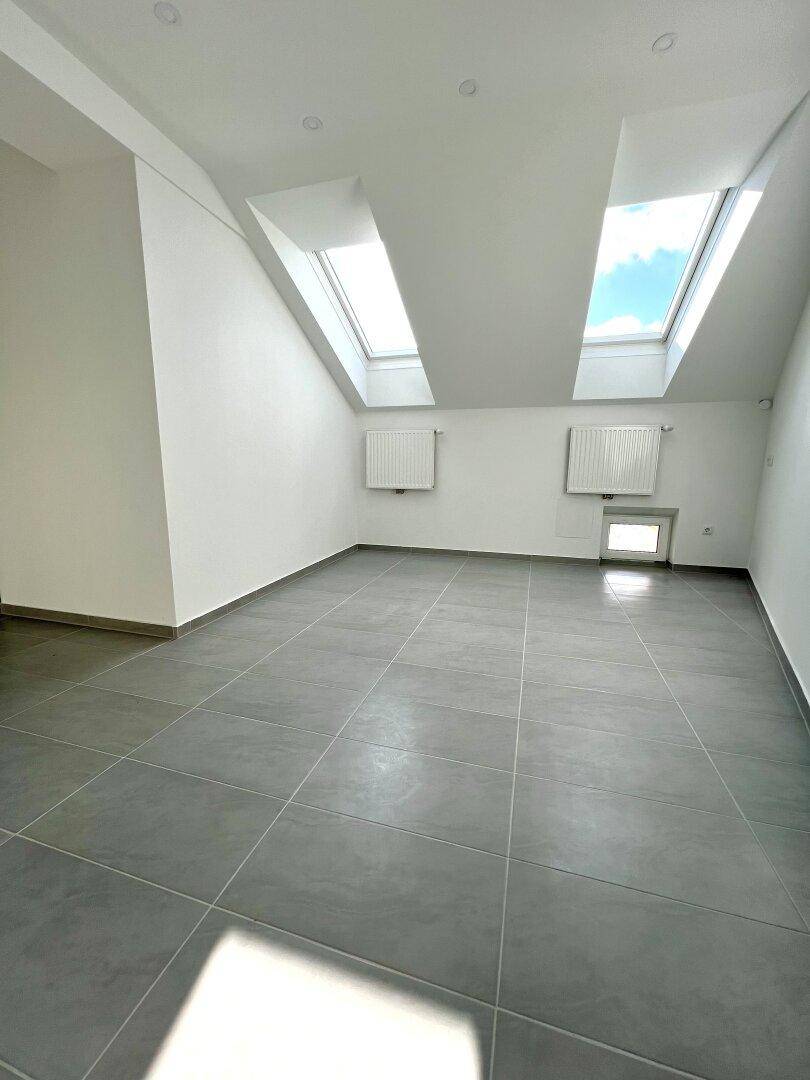 Helles Zimmer mit Fliesenboden und zwei Dachfenstern, ideal als Schlaf- oder Arbeitszimmer.