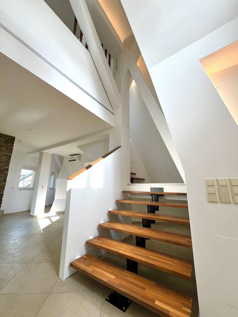 Elegante Holztreppe in einem hellen, offenen Flurbereich mit modernen Lichtakzenten.