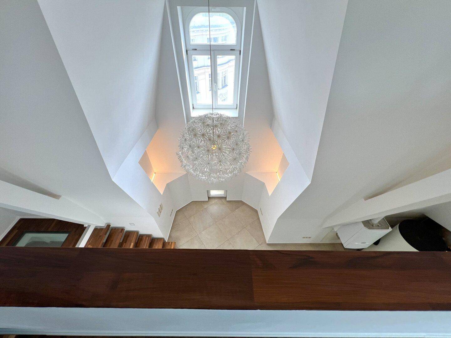 Blick von oben auf die offene Treppe und den hellen Wohnbereich mit Kronleuchter.