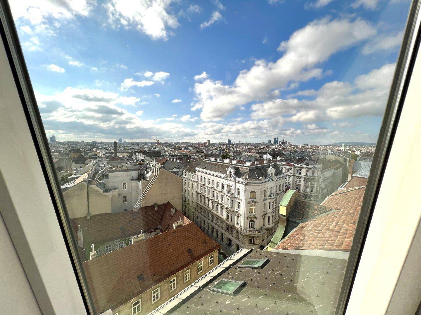 Panoramablick auf die Stadt Wien durch ein großes Fenster, mit weitem Horizont.