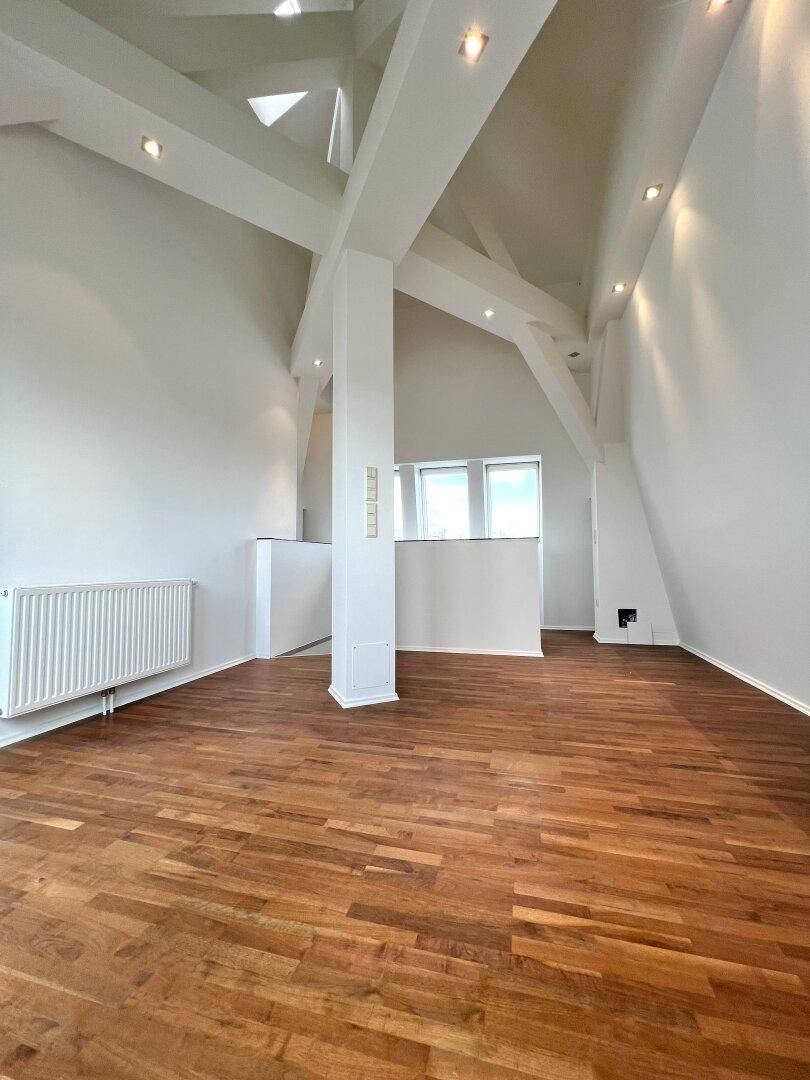 Geräumiges Wohnzimmer mit Holzboden und sichtbaren Dachbalken, bietet viel Tageslicht.