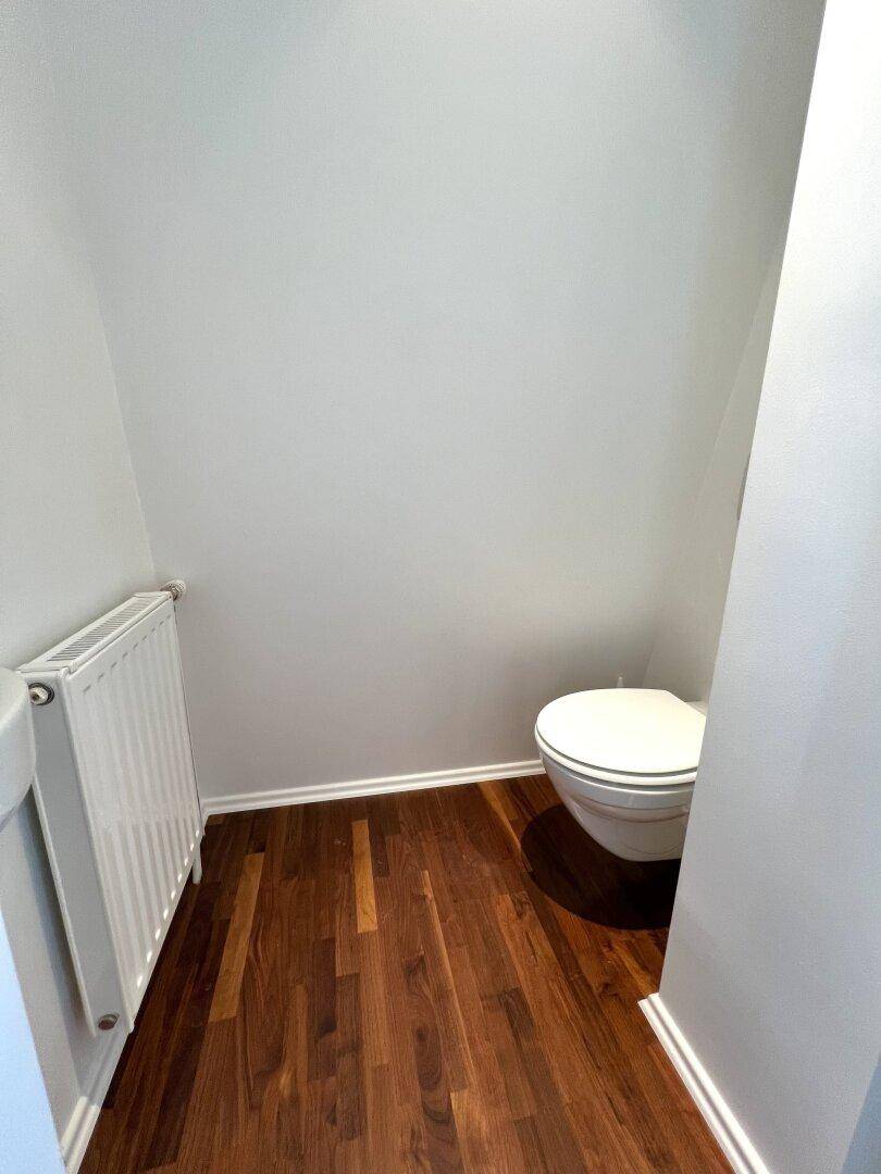 Kleines Gäste-WC mit Wand-WC und Heizkörper, mit dunklem Holzboden.