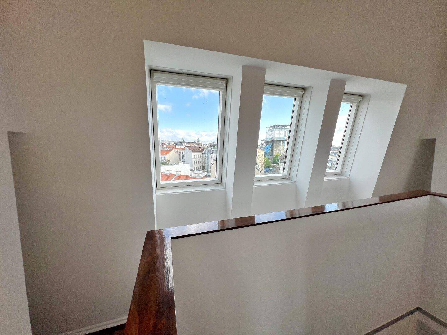 Heller Flurbereich mit Fenstern und Blick auf die Stadt, mit Holzgeländer.