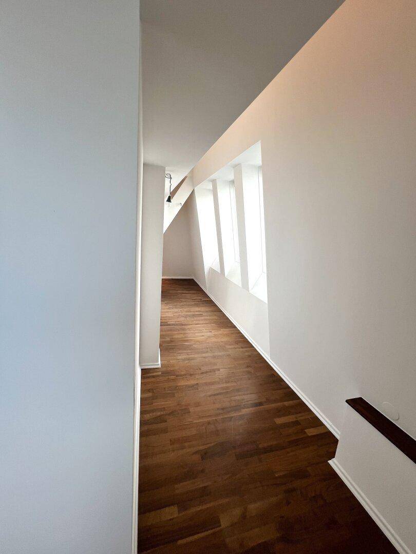 Langer, heller Flur mit Holzboden und Fenstern, die viel Tageslicht hereinlassen.