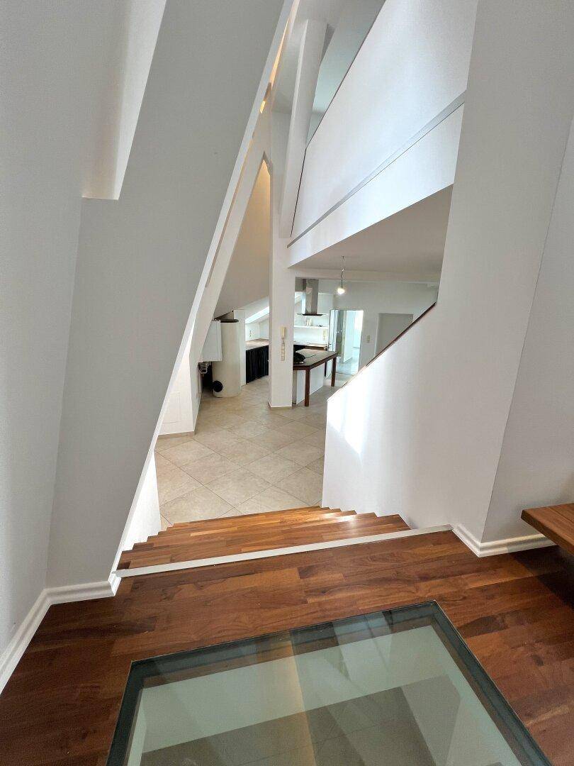 Blick von der Treppe in den offenen Wohnbereich mit Küche und hohen Decken.