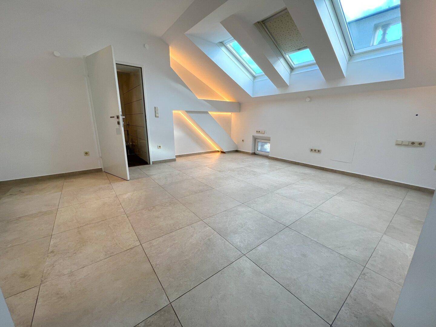 Geräumiges Zimmer mit Fliesenboden und mehreren Dachfenstern, sehr hell.