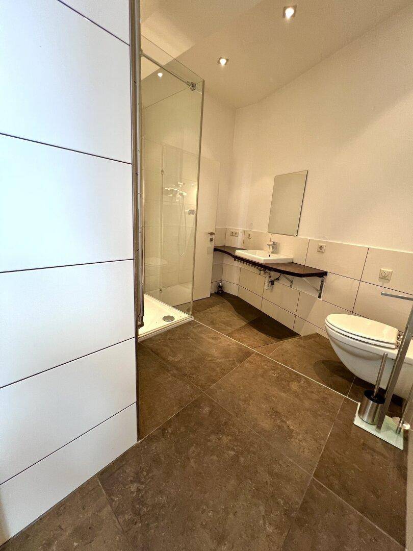 Modernes Badezimmer mit ebenerdiger Dusche, Hänge-WC und braunen Fliesenboden.