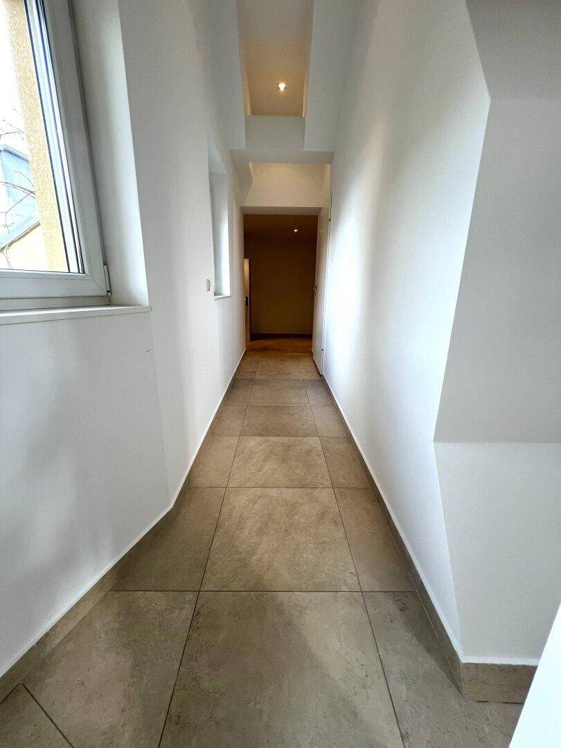 Heller, langer Flur mit Fliesenboden und Fenster, der zu weiteren Räumen führt.