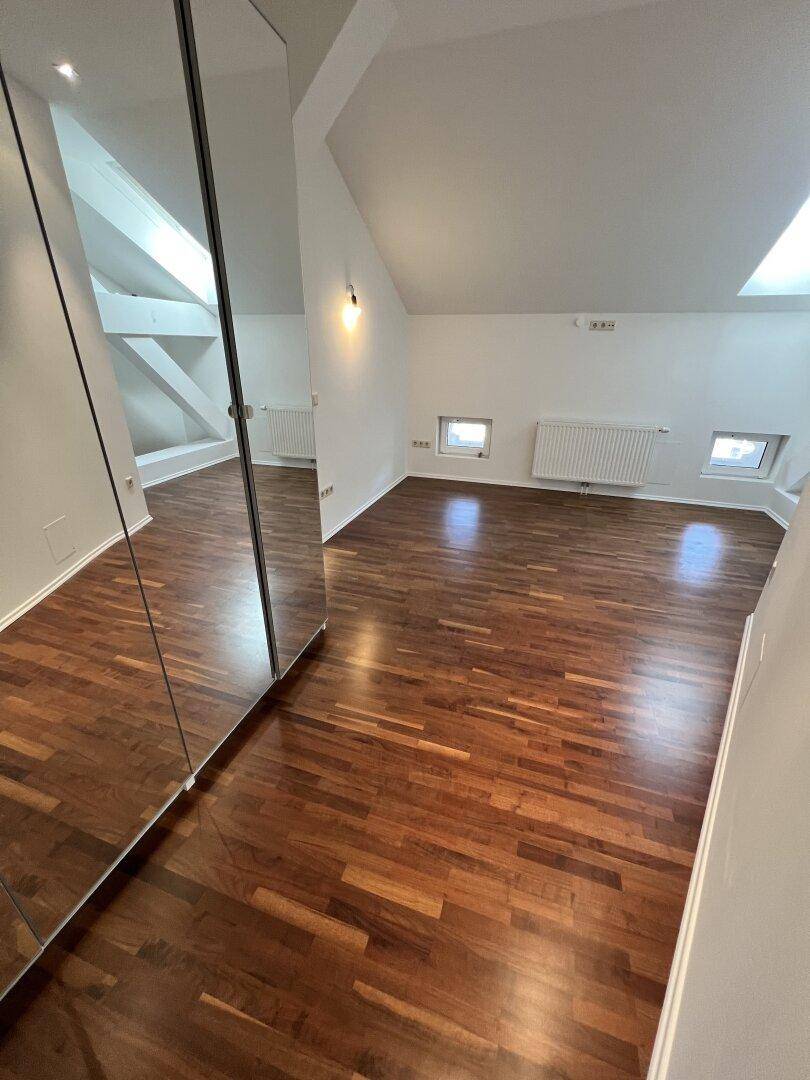 Helles Zimmer mit Holzboden und Spiegelfronten, unter Dachschrägen gelegen.