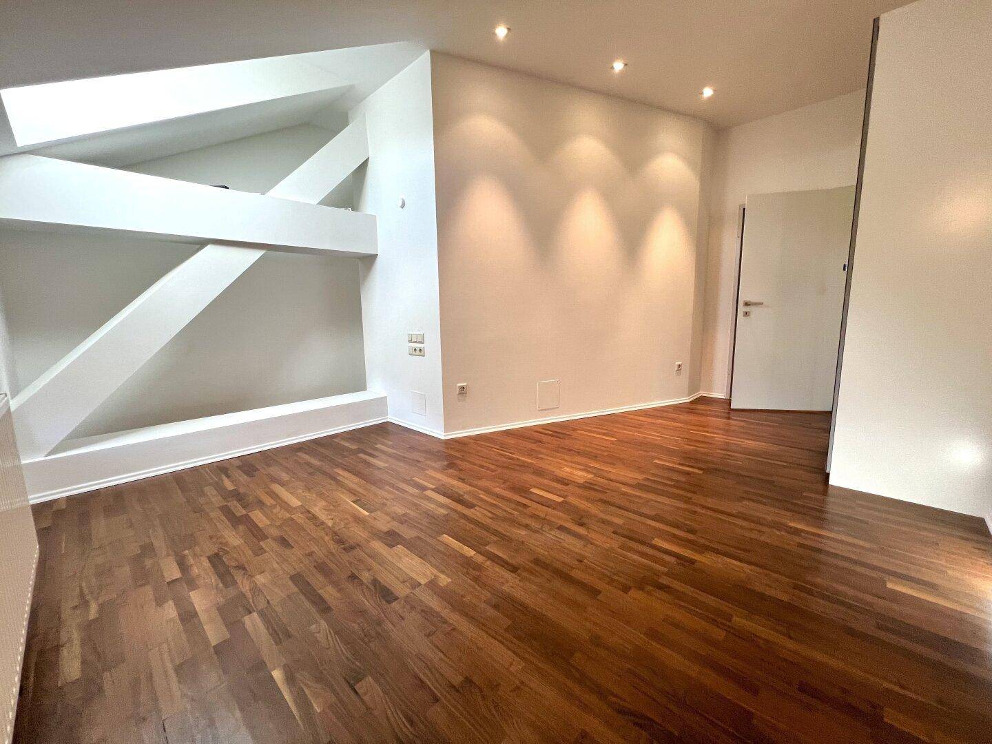 Geräumiges Zimmer mit Holzboden und indirekter Beleuchtung, unter Dachschrägen.