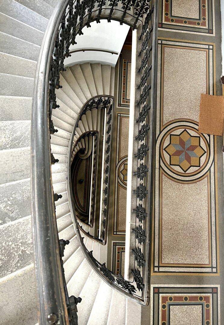 Elegantes Treppenhaus mit kunstvollem Geländer und dekorativem Mosaikboden in einem Altbau.