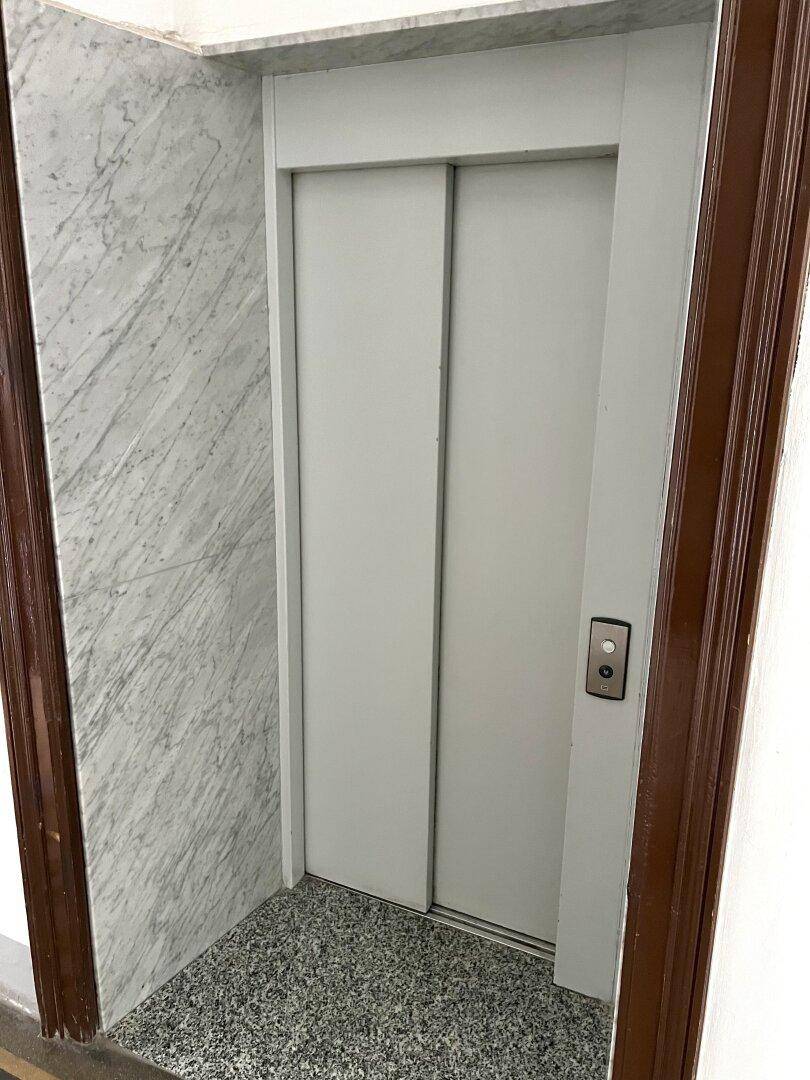 Moderner Aufzug mit Marmorverkleidung in einem eleganten Treppenhaus eines Altbaus.