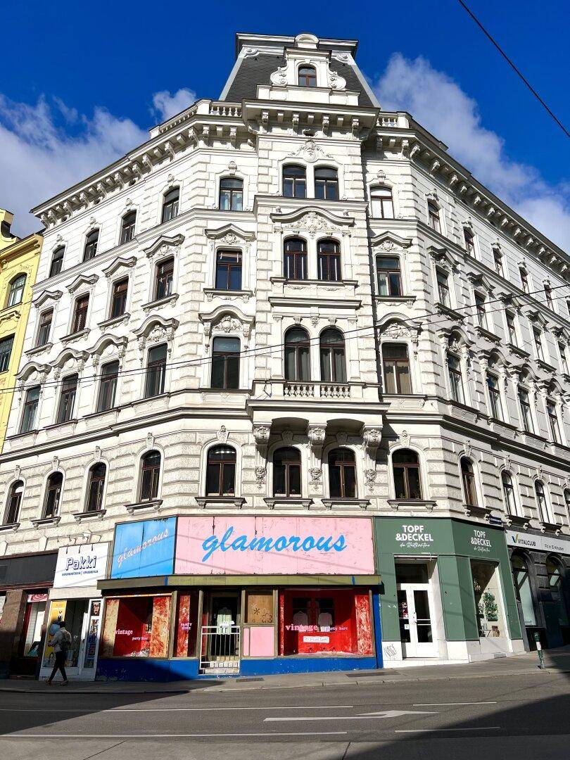 Historisches Gebäude mit reich verzierter Fassade und Geschäften im Erdgeschoss.