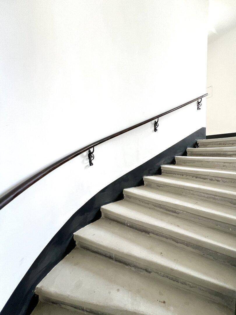 Gepflegtes Treppenhaus mit geschwungener Steintreppe und einem schlichten, dunklen Handlauf.