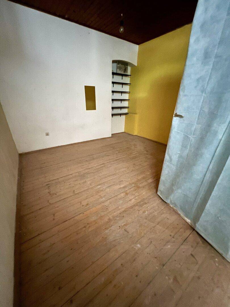 Leerer Raum mit gelber Wand, Holzdielenboden und einer Nische mit Regalen, bereit zur Renovierung.