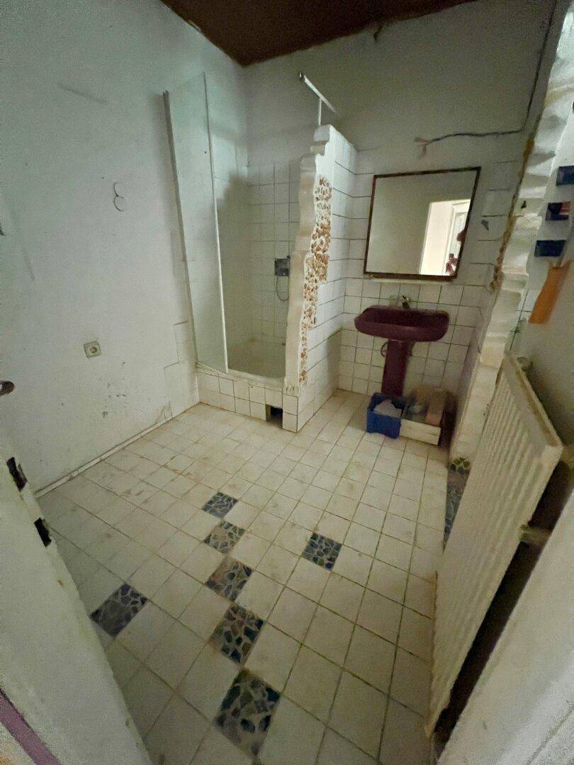 Badezimmer mit Duschbereich, Waschbecken und älteren Fliesen, das eine Renovierung benötigt.