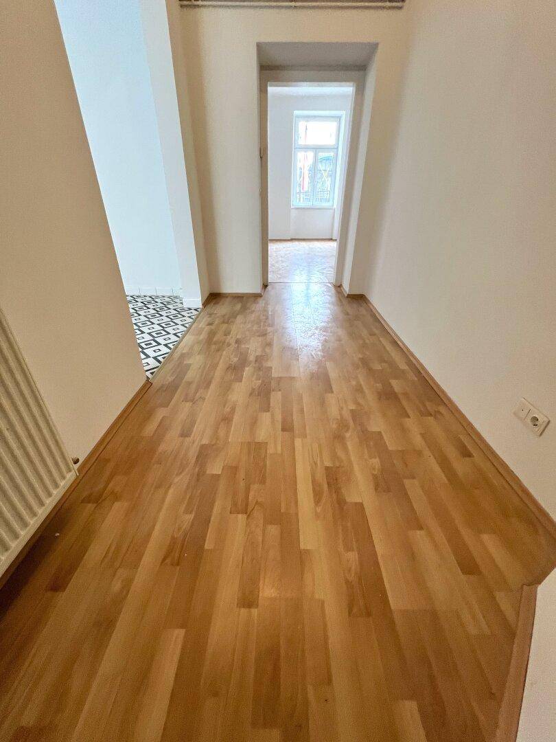 Langer, heller Flur mit Holzparkettboden, der zu einem weiteren Zimmer führt.