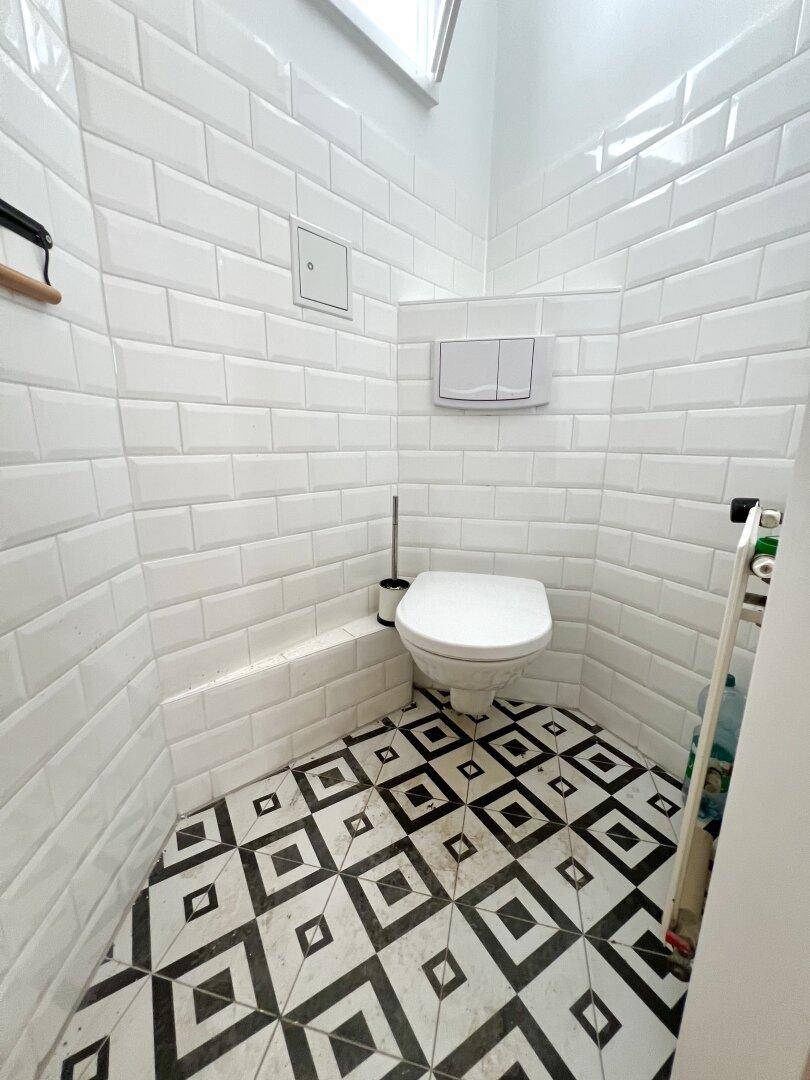 Separate Toilette mit weißen Wandfliesen und einem markanten schwarz-weißen Fliesenboden.
