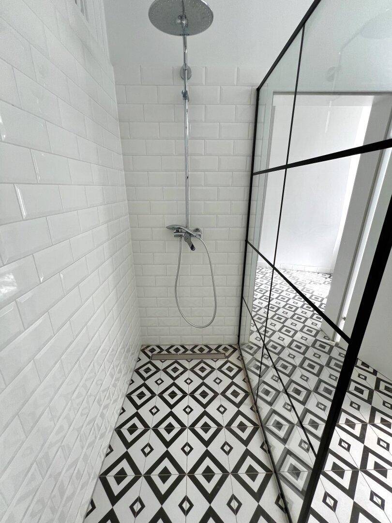 Detaillierte Ansicht der modernen Duschkabine mit Regendusche und auffälligem Fliesenboden.