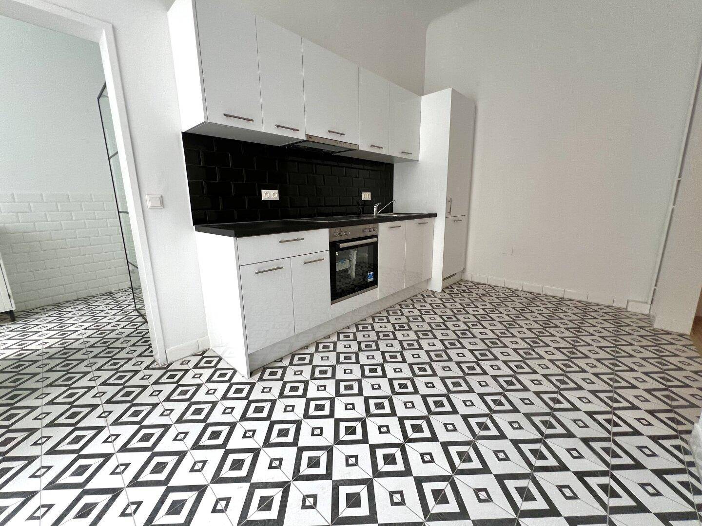Moderne Küche mit weißen Schränken, schwarzer Arbeitsplatte und auffälligem Fliesenboden.