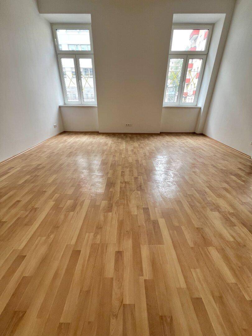 Geräumiges Zimmer mit schrägen Wänden, Parkettboden und zwei großen Fenstern.